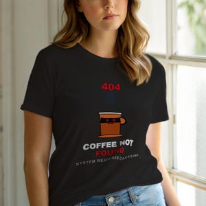 Może przedstawiać: Czarny t-shirt z grafiką filiżanki kawy. Grafika zawiera tekst "404", parę, filiżankę kawy z maską na oczy oraz słowa "COFFEE NOT FOUND" i "SYSTEM REQUIRES CAFFEINE".