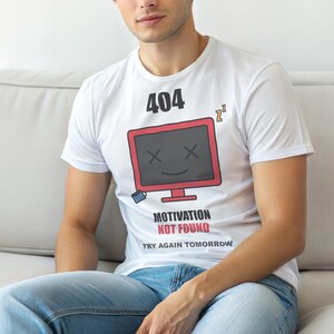 May include: White t-shirt with a red and black computer graphic and the text "404 Motivation Not Found Try Again Tomorrow". The graphic includes a sleeping symbol and a smiling computer screen with an X for eyes.