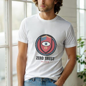 Peut inclure: T-shirt blanc avec un motif circulaire représentant un bouclier, un œil et un cadenas. Le texte "ZERO TRUST" est imprimé en dessous en noir et rose. Le t-shirt est porté par une personne.