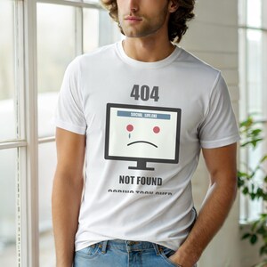 Może przedstawiać: Biała koszulka z grafiką ekranu komputera przedstawiającą smutną twarz, tekst "404 NOT FOUND" i "SOCIAL LIFE.EXE". Koszulka ma krótkie rękawy i okrągły dekolt.