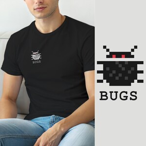 Op de afbeelding: Een zwart t-shirt met korte mouwen en een kleine pixel art afbeelding op de linkerborst. De afbeelding toont een gestileerd zwart insect met rode ogen en het woord BUGS in witte hoofdletters direct onder het icoon van het insect.