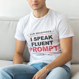 以下が含まれることがあります： 「LLM Whisperer - I Speak Fluent Prompt」の文字が黒と赤でプリントされた白いTシャツ。ソファに座っている人が着ています。下には「{HUMAN <-> AI}」と書かれています。