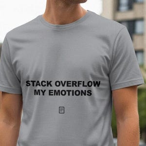 May include: A pale grey t-shirt featuring the black text "STACK OVERFLOW MY EMOTIONS" and a small graphic. The short-sleeved shirt is likely made from a soft fabric.