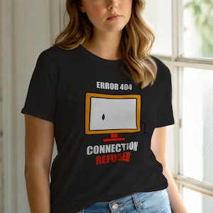 Puede incluir: Camiseta negra con un diseño de pantalla de ordenador. El texto "ERROR 404" está encima de la pantalla y "CONNECTION REFUSED" debajo. La pantalla es blanca con un punto negro y un borde naranja. El texto es blanco y rojo.