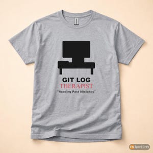 Può includere: T-shirt grigio con grafica di computer nera e la scritta "GIT LOG THERAPIST" in nero e rosa. Sotto il testo c'è la citazione "Reading Past Mistakes". La maglietta è realizzata in un materiale morbido.