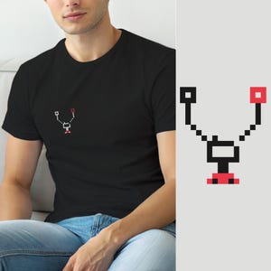 Puede incluir: Una camiseta negra de manga corta con un pequeño gráfico de pixel art centrado en el pecho. El diseño consiste en una estructura en forma de Y de color negro y rojo con una base cuadrada, que recuerda a un componente electrónico simple.