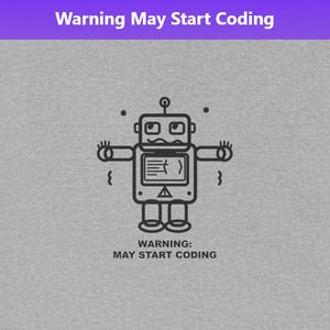 Op de afbeelding: Een grijs t-shirt met een zwart-wit robotafbeelding en de tekst "Warning May Start Coding" boven en onder de robot. De robot heeft een scherm op zijn borst en uitgestrekte armen.