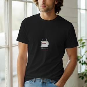May include: Black crew neck t-shirt with a minimalist coffee cup graphic. The white cup has a red stripe design and the words "SELECT COFFEE" in red below it. The shirt is made of a soft material.