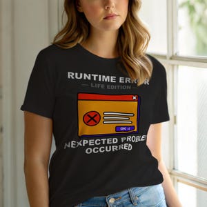 May include: Black t-shirt with a graphic of a computer error message. The text reads "RUNTIME ERROR - LIFE EDITION" above a yellow and orange error window with an X and the text "OK :(". Below the window, the text reads "NEXPECTED PROBLEM OCCURRED".