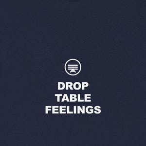 Może przedstawiać: Granatowa koszulka z białym napisem "DROP TABLE FEELINGS" pod okrągłą grafiką. Koszulka z krótkim rękawem jest w jednolitym kolorze.