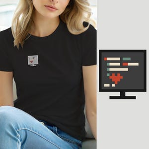 Op de afbeelding: Een zwart T-shirt met korte mouwen en een kleine geborduurde afbeelding op de borst. De afbeelding toont een computermonitor met regels code en een gepixeld rood hartpictogram in het midden van het scherm.