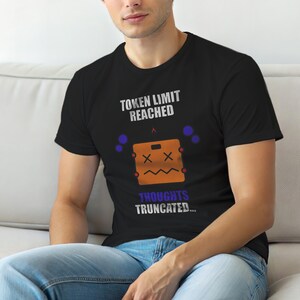 Puede incluir: Camiseta negra con el texto "TOKEN LIMIT REACHED" sobre un cuadrado naranja de dibujos animados con ojos en "X" y una boca en zigzag. El texto "THOUGHTS TRUNCATED..." está debajo.