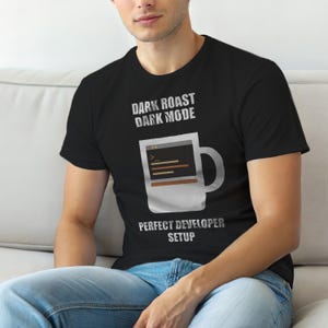 May include: Black t-shirt with the text "DARK ROAST DARK MODE" above a white mug graphic with a computer code display. Below the mug is the text "PERFECT DEVELOPER SETUP".