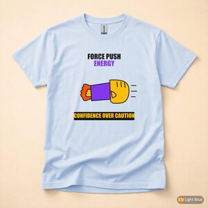Könnte beinhalten: Hellblaues T-Shirt mit den Worten "FORCE PUSH ENERGY" über einer Cartoon-Grafik einer Faust. Unter der Grafik steht der Text "CONFIDENCE OVER CAUTION". Das T-Shirt hat eine hellblaue Farbe.