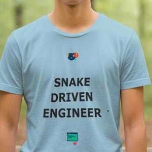 Op de afbeelding: Lichtblauw t-shirt met de zwarte tekst "SNAKE DRIVEN ENGINEER". Het shirt heeft een kleine afbeelding boven en onder de tekst. De achtergrond is een vage bosscène.