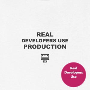 May include: White t-shirt with the text "REAL DEVELOPERS USE PRODUCTION" in black. Below the text is a small graphic and a pink circle with the words "Real Developers Use".