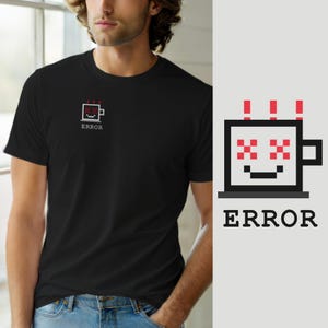 May include: A black short-sleeved t-shirt featuring a small pixel art graphic on the left chest. The graphic depicts a square mug with red pixelated eyes, a black mouth, and three red vertical lines above it, with the word ERROR printed below.