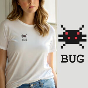 Może przedstawiać: Biały t-shirt z krótkim rękawem z małą, pikselową grafiką czarnego owada z czterema czerwonymi kwadratowymi oczami na klatce piersiowej. Pod owadem znajduje się napis BUG wydrukowany prostą czarną czcionką bezszeryfową, wyśrodkowany na górze.