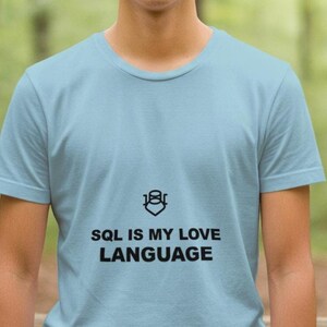 May include: Light blue t-shirt with the text "SQL IS MY LOVE LANGUAGE" in black. The shirt features a graphic above the text. The t-shirt is made of a soft material and has short sleeves.