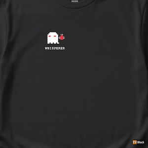 Puede incluir: Camiseta negra con un diseño de fantasma blanco pixelado y detalles rojos, con la palabra "Whisperer" debajo. El gráfico está centrado. La camiseta está hecha de algodón grueso.
