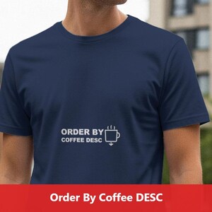 Może przedstawiać: Granatowa koszulka z napisem "ORDER BY COFFEE DESC" i grafiką filiżanki kawy w kolorze białym. Koszulka ma okrągły dekolt i krótkie rękawy.