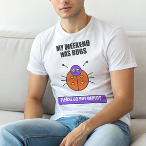 Puede incluir: Camiseta blanca con el texto "MY WEEKEND HAS BUGS" y una ilustración de una mariquita de dibujos animados. Debajo de la mariquita está el texto "PLEASE DO NOT DEPLOY". La mariquita es naranja con ojos morados y una cara triste.