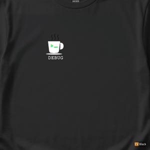 Puede incluir: Camiseta negra con un gráfico blanco de una taza de café con vapor, una flecha verde y la palabra "DEBUG" debajo. La camiseta está hecha de algodón grueso.