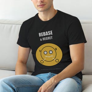 Puede incluir: Camiseta negra con el texto "REBASE & REGRET" sobre un gráfico de carita sonriente amarilla distorsionada. El gráfico tiene dos ojos, una boca curvada y dos pequeños círculos a cada lado.