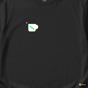 Puede incluir: Camiseta negra con un diseño de taza de café blanca, puntos verdes y vapor. El diseño es minimalista y moderno. La camiseta es de algodón grueso, ideal para uso casual.
