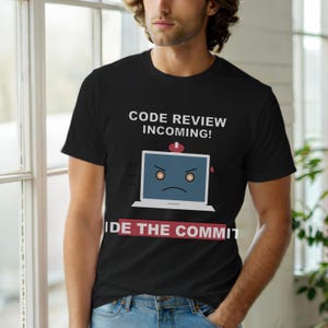 Puede incluir: Camiseta negra con el texto "CODE REVIEW INCOMING!" sobre un portátil de dibujos animados con una cara triste. Debajo del portátil hay una pancarta roja con el texto "IDE THE COMMIT". La camiseta es de material suave.