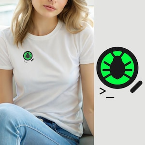 Könnte beinhalten: Ein weißes kurzärmeliges T-Shirt mit einer kleinen Grafik auf der linken Brust. Die Grafik besteht aus einer schwarzen kreisförmigen Umrandung mit einer leuchtend grünen Insektensilhouette sowie einem kleinen schwarzen Strich und einem Größer-als-Zeichen.