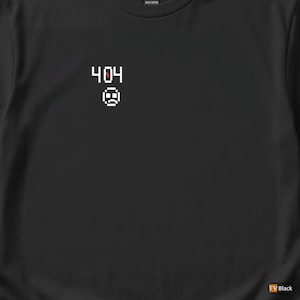 Może przedstawiać: Czarny t-shirt z pikselowym wzorem. Wzór zawiera numer "404" nad smutną emotikoną. Koszulka wykonana jest z ciężkiego materiału bawełnianego.