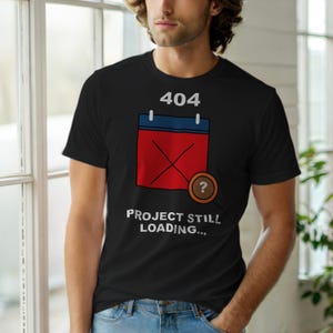May include: Black t-shirt with a humorous graphic. The design features a red calendar with an X, the number 404 above it, and the text "PROJECT STILL LOADING..." in white. A question mark is next to the calendar.