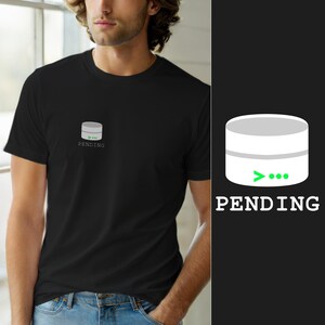 Peut inclure: Un t-shirt noir à manches courtes avec un petit motif sur la poitrine. Le motif représente un récipient cylindrique gris stylisé avec une icône de chargement verte et le mot PENDING imprimé en lettres capitales blanches en dessous.