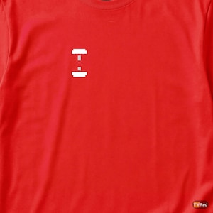 Puede incluir: Una camiseta roja brillante con un gráfico blanco pixelado de una barra con pesas. El diseño está centrado en el pecho. La camiseta está hecha de un material suave.