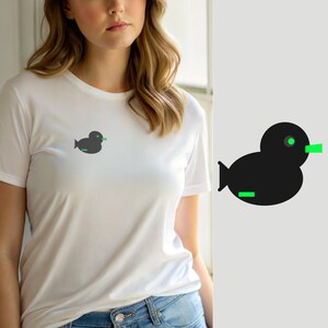 Op de afbeelding: Een wit T-shirt met korte mouwen en een kleine, minimalistische zwarte eend-afbeelding op de linkerborst. Het eendontwerp bevat een fel neongroen oog, een neongroene snavel en een horizontale neongroene lijn op het onderlichaam.