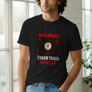 以下が含まれることがあります： 黒いTシャツ。茶色のコーヒーカップのグラフィックで、赤いアクセントと湯気が描かれています。「STACK TRACE INCLUDED」の文字が白と赤でカップの下にプリントされています。