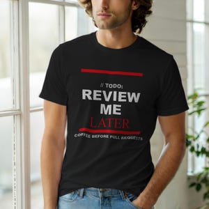 Puede incluir: Camiseta negra de cuello redondo con texto blanco y rojo. El texto dice "// TODO: REVIEW ME LATER COFFEE BEFORE PULL REQUESTS". La camiseta tiene un diseño sencillo y probablemente está hecha de algodón.