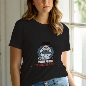 May include: Black t-shirt with a cartoon design of a figure in a hat and the text "KUBERNETES WHISPERER" and "PODS FEAR ME". The design is in blue, white, and black. The shirt is made of a soft material.