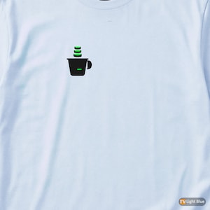 Op de afbeelding: Lichtblauwe longsleeve met een kleine afbeelding van een zwarte koffiekop met groene stoom. Het shirt is gemaakt van een zacht materiaal en is geschikt voor vrijetijdskleding.