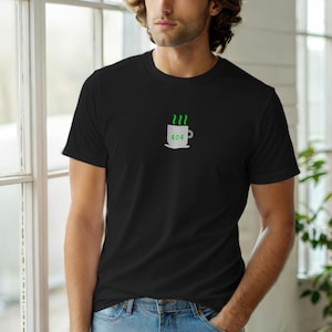 Może przedstawiać: Czarny t-shirt z białą grafiką filiżanki do kawy i numerem 404. Z filiżanki unosi się zielona para. T-shirt jest wykonany z miękkiego materiału.