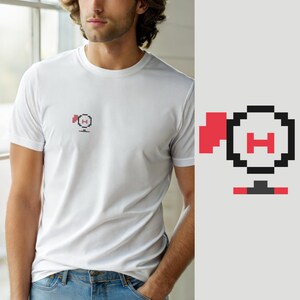 Puede incluir: Una camiseta blanca de manga corta con un pequeño gráfico de pixel art en el pecho izquierdo. El gráfico muestra un contorno circular negro con una letra H roja en el centro, una bandera roja a la izquierda y una base horizontal roja.