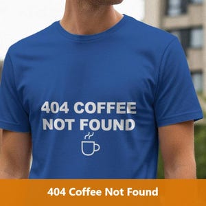 May include: A royal blue t-shirt featuring the white text "404 COFFEE NOT FOUND" and a white coffee cup graphic. The short-sleeved shirt is likely made of a soft fabric. The image is taken outside, with a building in the background.