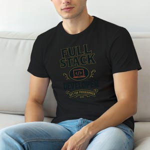 Op de afbeelding: Een zwart t-shirt met korte mouwen en de tekst FULL STACK DEVELOPER in een gestileerd lettertype. Onder de tekst staat een afbeelding van een laptop met code-haakjes en een banner met de tekst GIFT FOR PROGRAMMER.