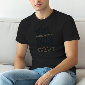 May include: A black short-sleeved t-shirt featuring the text "SQL IS MY SUPER POWER" in a dark blue font with gold accents. The design includes a small gold lightning bolt icon inside an oval shape at the bottom of the graphic print.