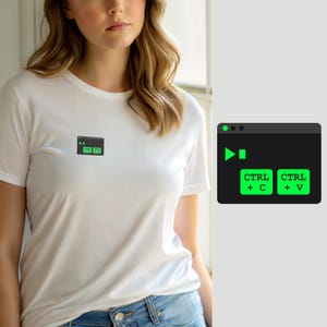 May include: A white short-sleeved t-shirt featuring a small graphic on the chest. The graphic is a dark grey rectangular window containing a bright green play icon and two green buttons labelled CTRL + C and CTRL + V in black text.