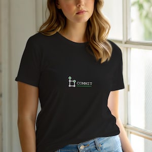 Puede incluir: Camiseta negra con la palabra "COMMIT" en blanco y verde. El diseño incluye un gráfico estilizado encima del texto. La camiseta es de manga corta y parece estar hecha de un material suave.
