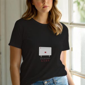 Op de afbeelding: Zwart T-shirt met een witte afbeelding van een computerscherm, een rood vierkant en drie stippen. De rode tekst "FRONTEND LIES" staat eronder. Het T-shirt is gemaakt van zacht materiaal.
