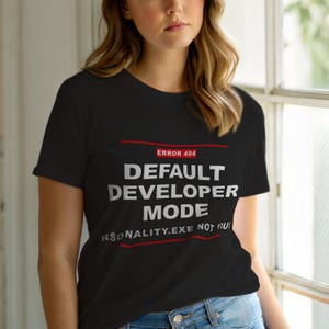 May include: Black t-shirt with white text that reads "DEFAULT DEVELOPER MODE" and "ERROR 404". The shirt also has the text "RSONALITY.EXE NOT FOU". The text is in a sans-serif font.