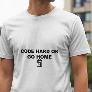 Puede incluir: Camiseta blanca con el texto negro "CODE HARD OR GO HOME" y un dibujo de una casa con un ordenador. La camiseta de manga corta está hecha de un tejido suave.